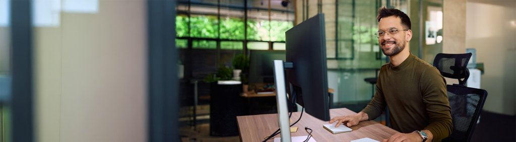 Ein junger Mann mit einer Brille sitzt an einem Monitor.