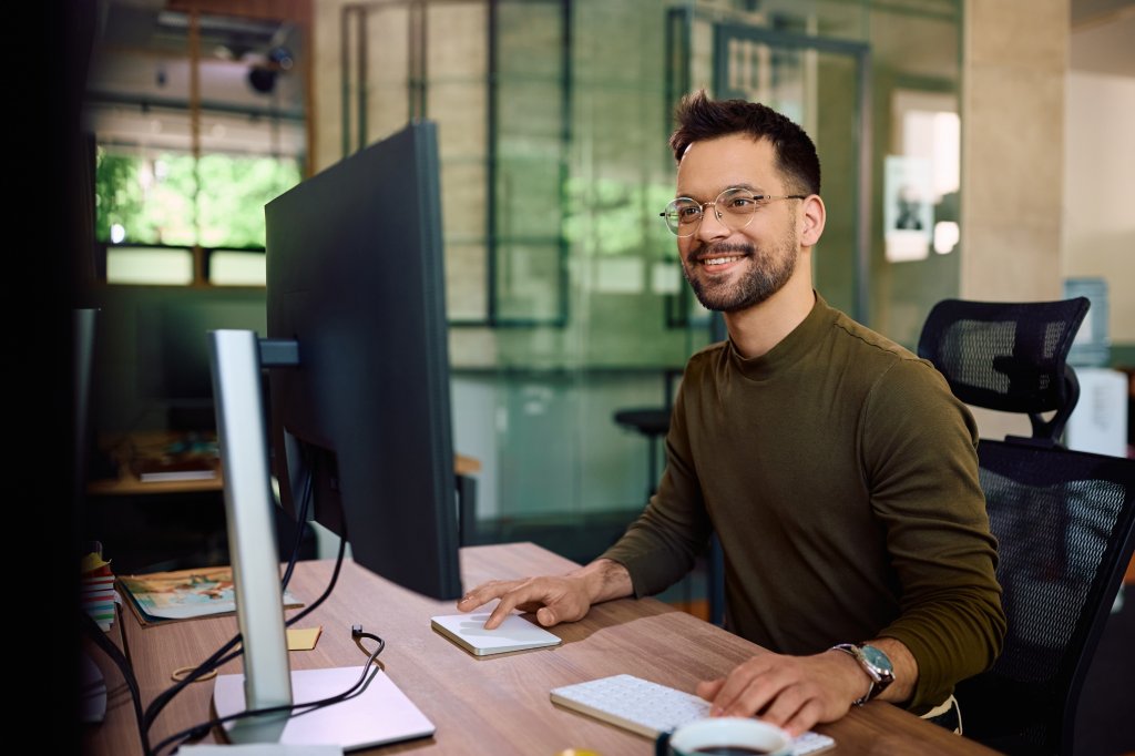 Ein junger Mann mit einer Brille sitzt an einem Monitor.